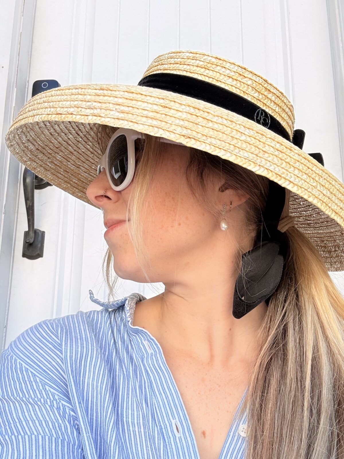 blonde woman wearing a large rimmed straw sunhat with black ribbon trim