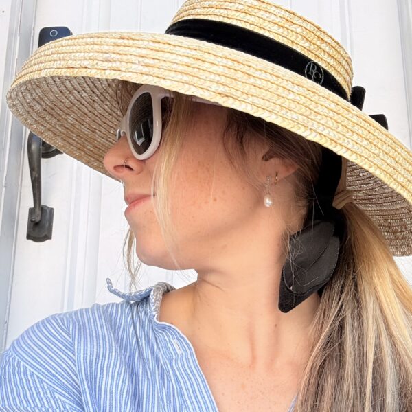 blonde woman wearing a large rimmed straw sunhat with black ribbon trim